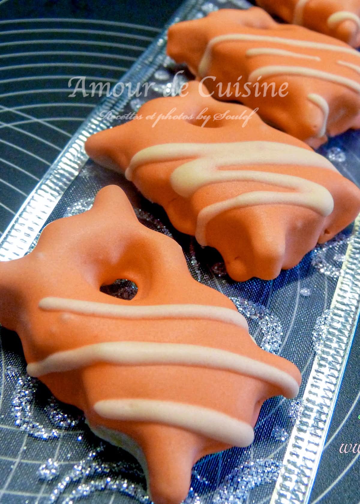 Biscuits sablés de Noël recouverts de glaçage royal orange avec des décorations blanches, disposés sur un plateau argenté. Gourmandises festives au design soigné et aux saveurs épicées, idéales pour les fêtes de fin d'année.