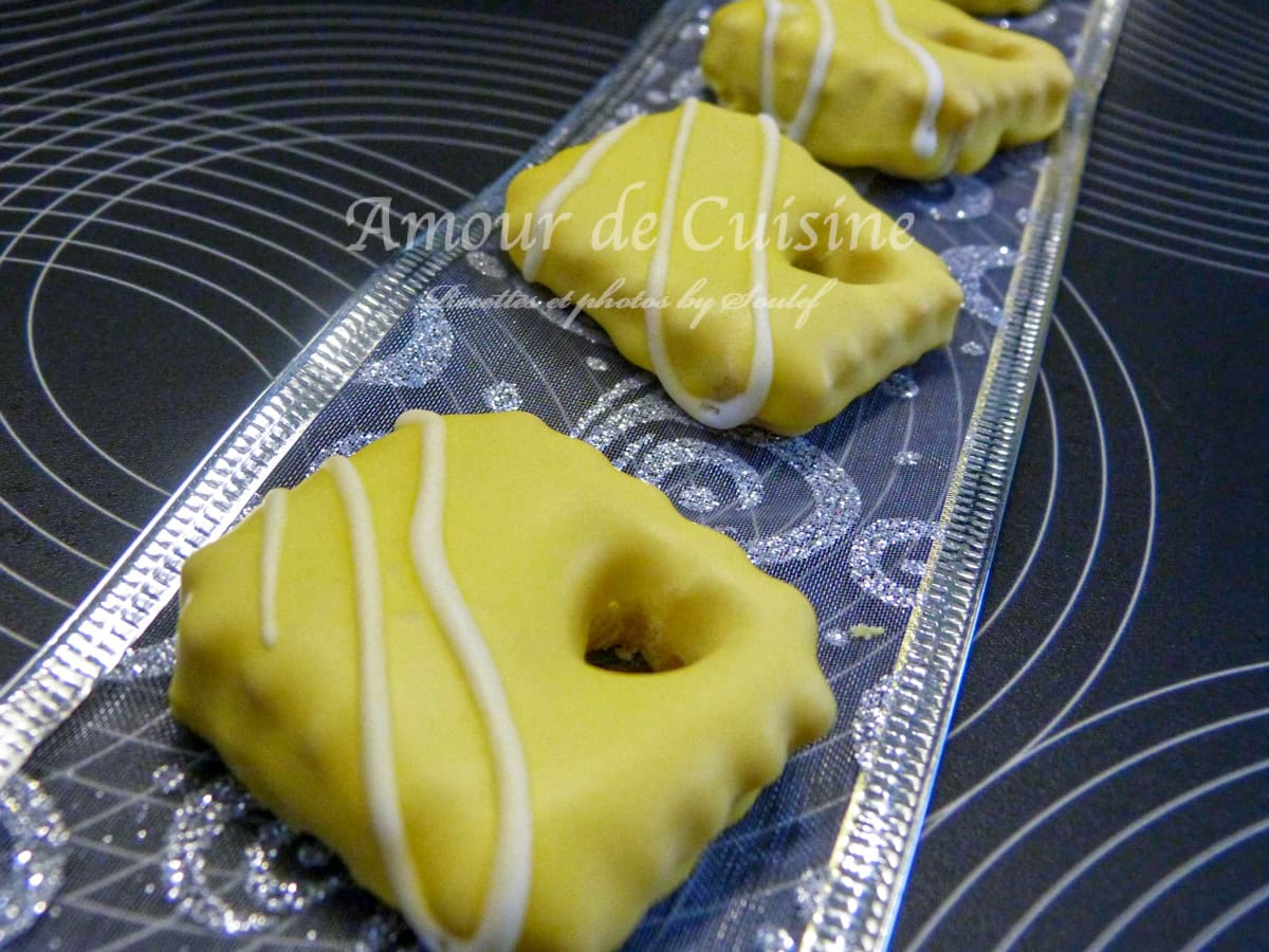 Biscuits sablés de Noël décorés avec un glaçage royal jaune et des motifs blancs, présentés sur un plateau élégant