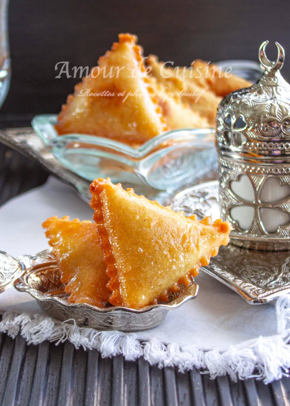 Samsa aux amandes dorée et nappée de miel, une pâtisserie algérienne croustillante et fondante. Servie sur un plateau oriental en métal argenté avec une touche d’élégance, parfaite pour accompagner un thé à la menthe. Recette traditionnelle du Ramadan et des fêtes