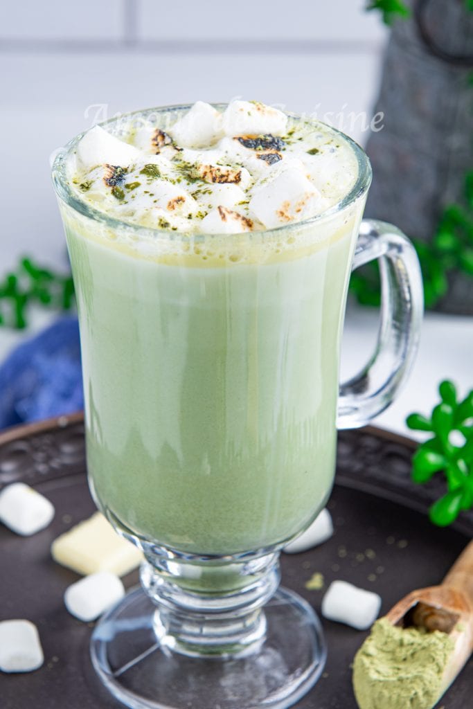 Chocolat chaud au matcha et chocolat blanc, servi dans un verre transparent, garni de mini marshmallows grillés et saupoudré de poudre de matcha